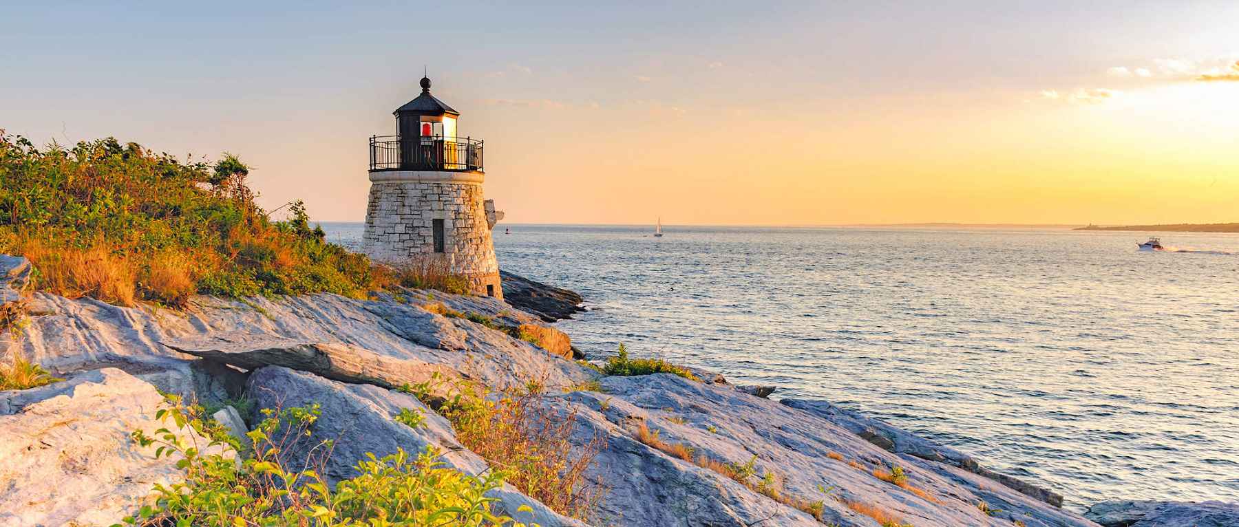 Castle Hill Light at sunset above the rocky Newport, Rhode Island coastline
